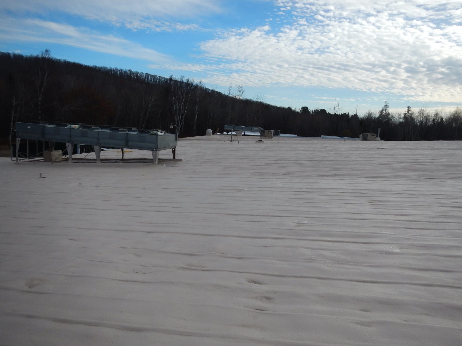 Applicator spraying polyurea roof coating on a metal panel roof